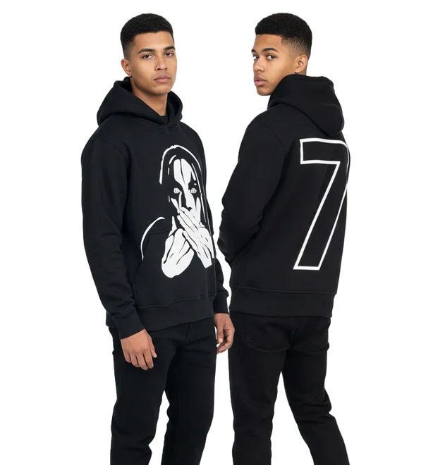 Young man wearing black hoodie with graphic face on front and large number 7 on back, standing in studio