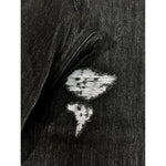 Close-up of black denim jeans with a frayed hole and light threads showing underneath