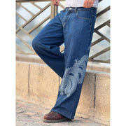 Person wearing blue wide-leg jeans with a detailed dragon print on the leg, brown boots, and white top