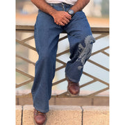 Person wearing blue jeans with a dragon design sitting on railing, wearing brown boots and a wristwatch